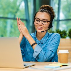 Jolie jeune femme caucasienne parlant au téléphone sur son ordinateur portable, un casque sur les oreilles, dans un bureau moderne